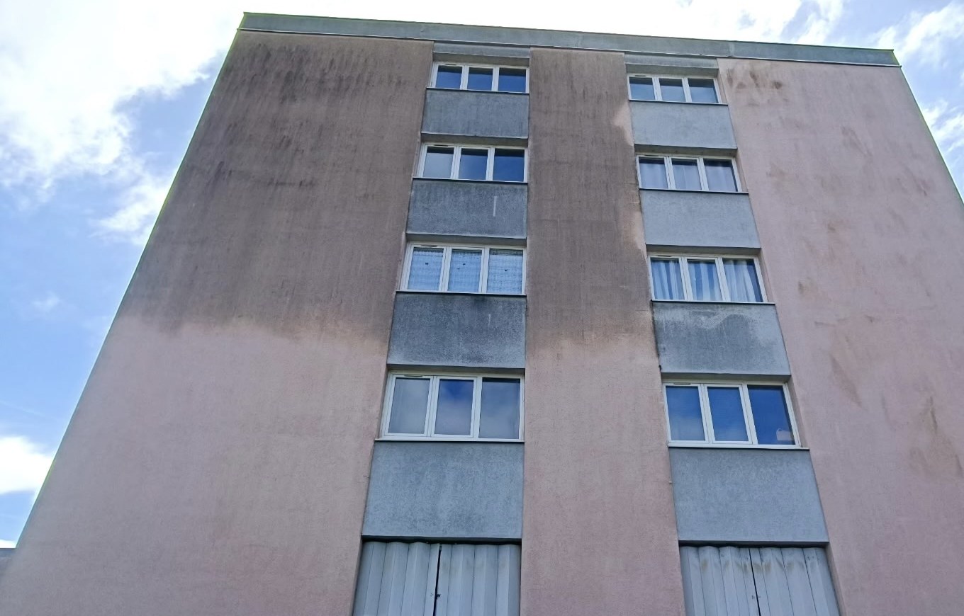 Façade d'immeuble à moitié nettoyée : partie claire traitée, partie grise encore à traiter